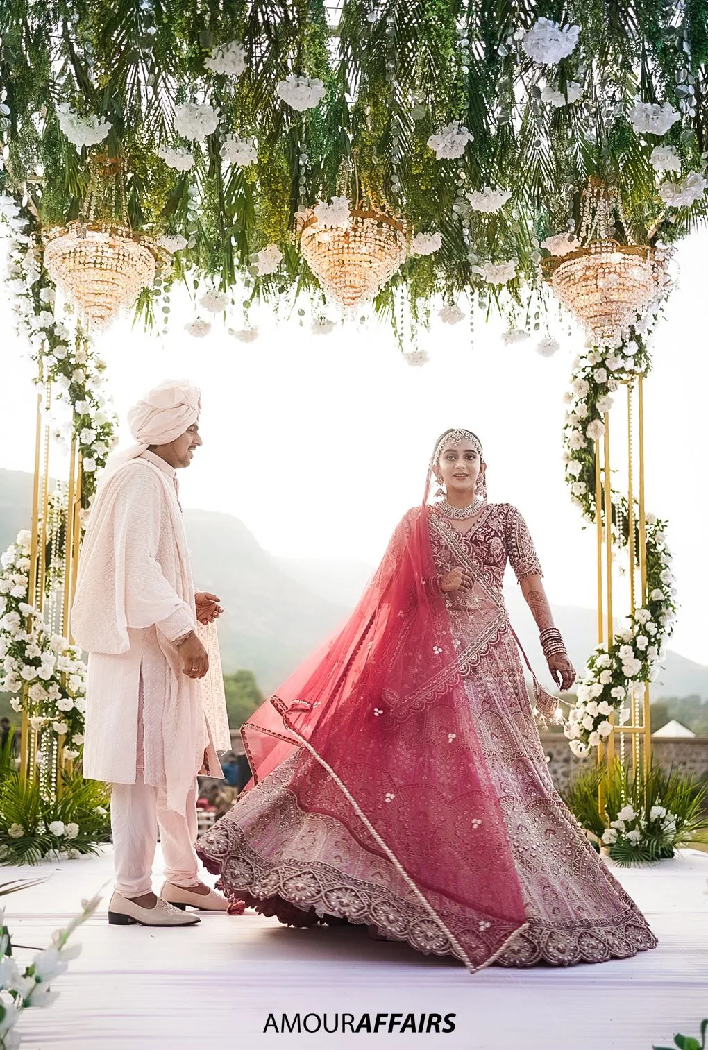 Candid wedding photograph of a bride twirling her lehenga at the mandap while the groom watches