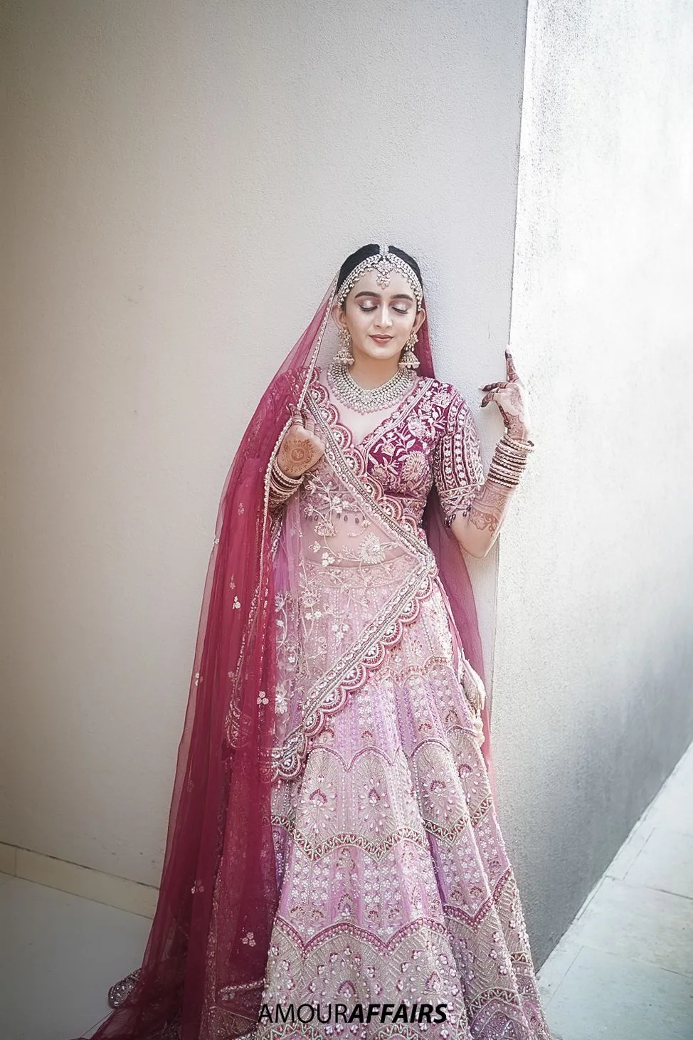 Bridal portrait of a bride in a pink embroidered lehenga and veil posing against a white wall