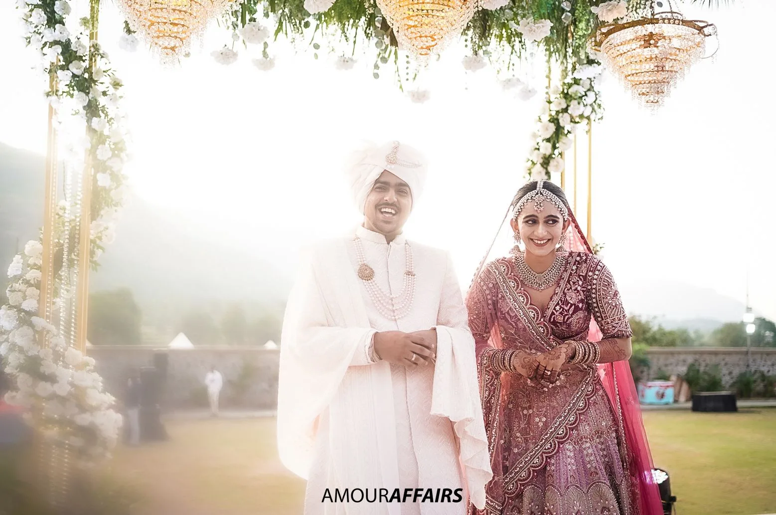 Bride and groom smiling together beneath a floral mandap in soft evening light at an outdoor wedding